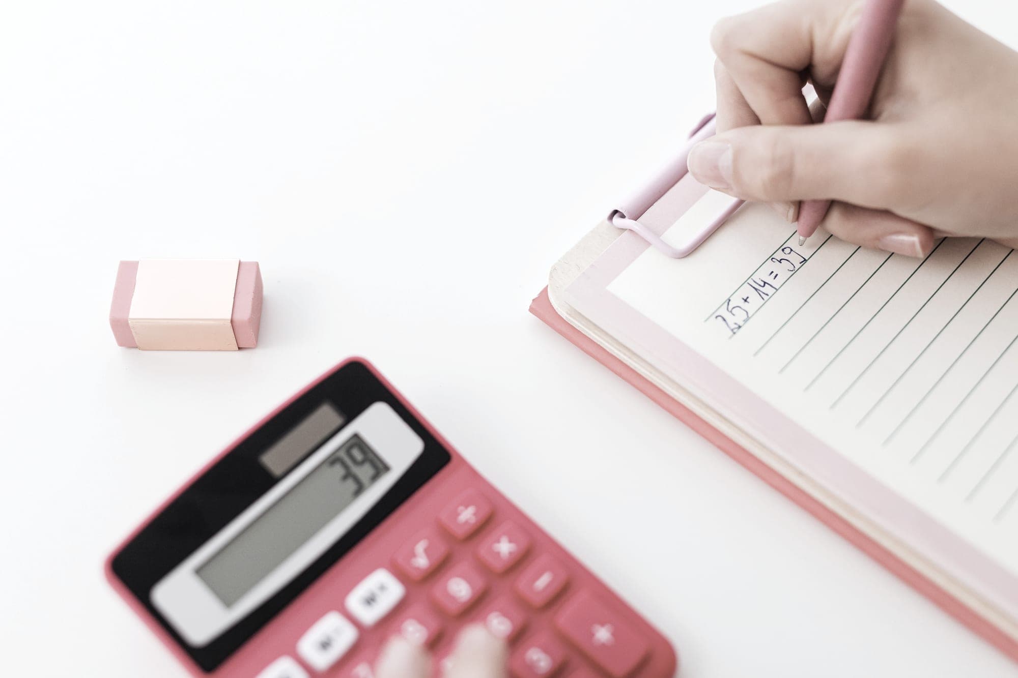 Hands using a calculator and writing figures in a notebook on a pale desk