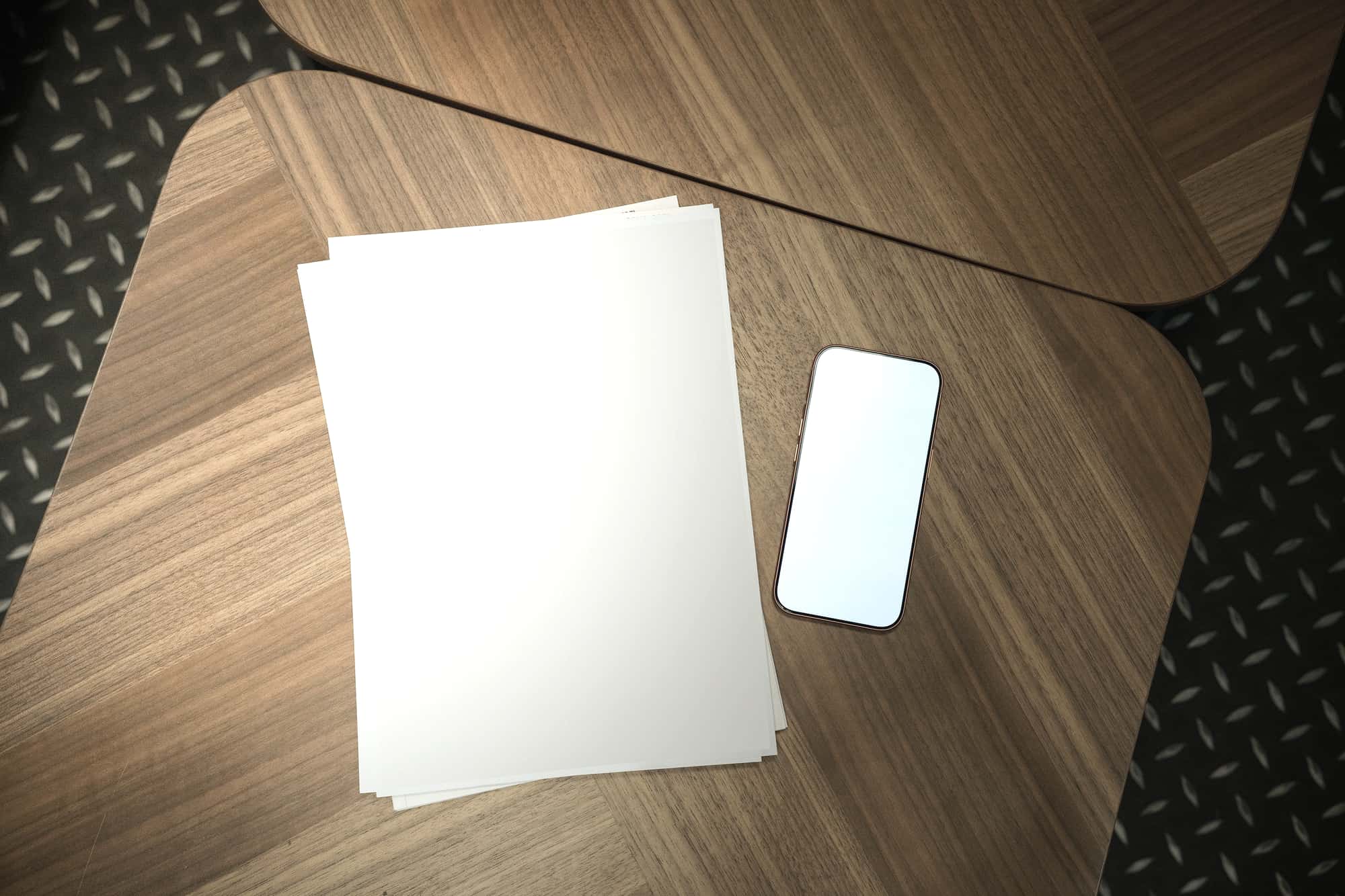 Blank sheets of paper and a phone on a pale wooden table, viewed from above